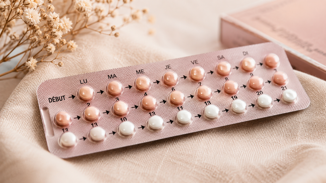 Plaquette de pilules contraceptives roses et blanches posée sur un tissu beige à côté de fleurs séchées, illustrant l'impact des hormones sur la libido féminine.
